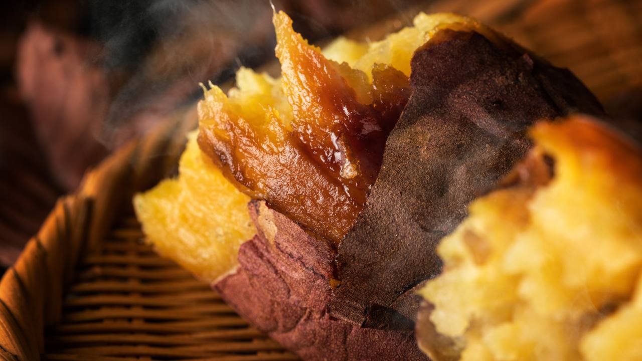 割れた焼き芋から湯気が立ち、黄金色のほくほくした中身と蜜がにじむ断面が見える画像