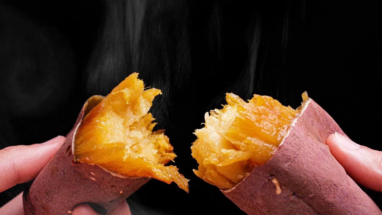 湯気の立つ焼き芋を両手で二つに割ったところの写真